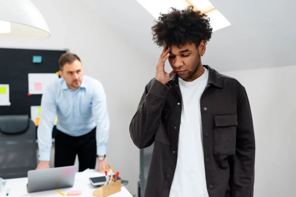 Two men standing in an office with one holding his head.