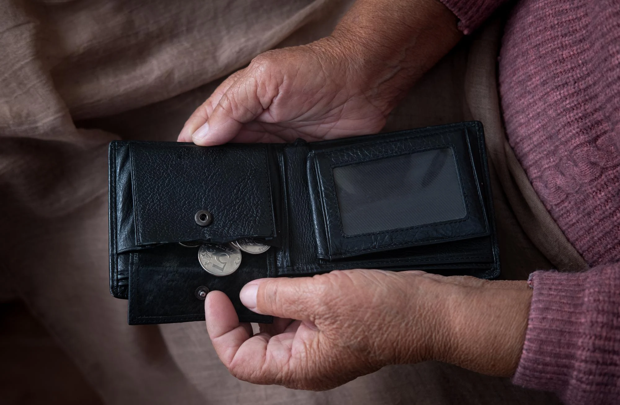 A woman's hand holding a black wallet with coins in it.