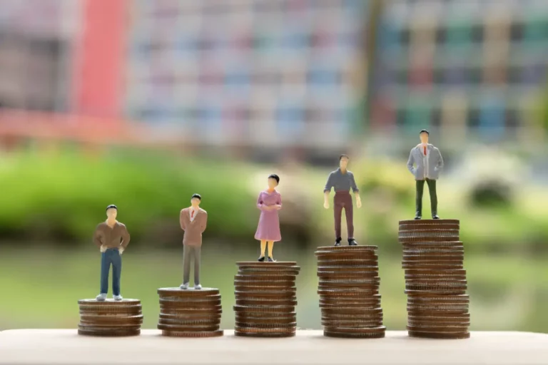 Miniature people standing on top of stacks of coins.