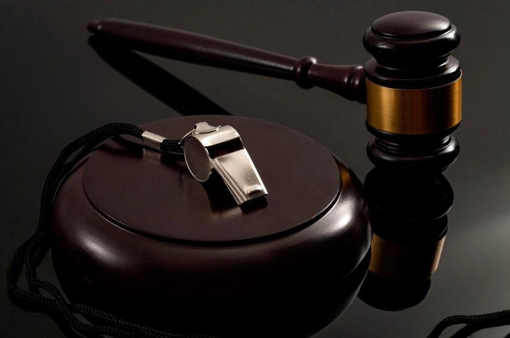 metal whistle and wooden judge gavel on a dark background conceptualizing whistleblower protection law