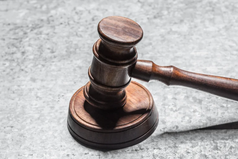 A wooden judge's gavel rests on a sound block on a textured gray surface.