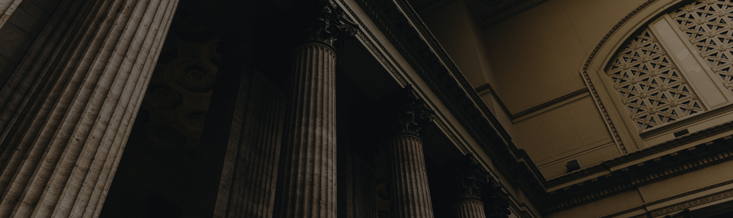 An interior view of a building featuring tall, classical columns under a dim light offers a solemn ambiance. The upper walls are decorated with intricate patterns and architectural details that evoke the meticulous care akin to employment litigation and counseling.