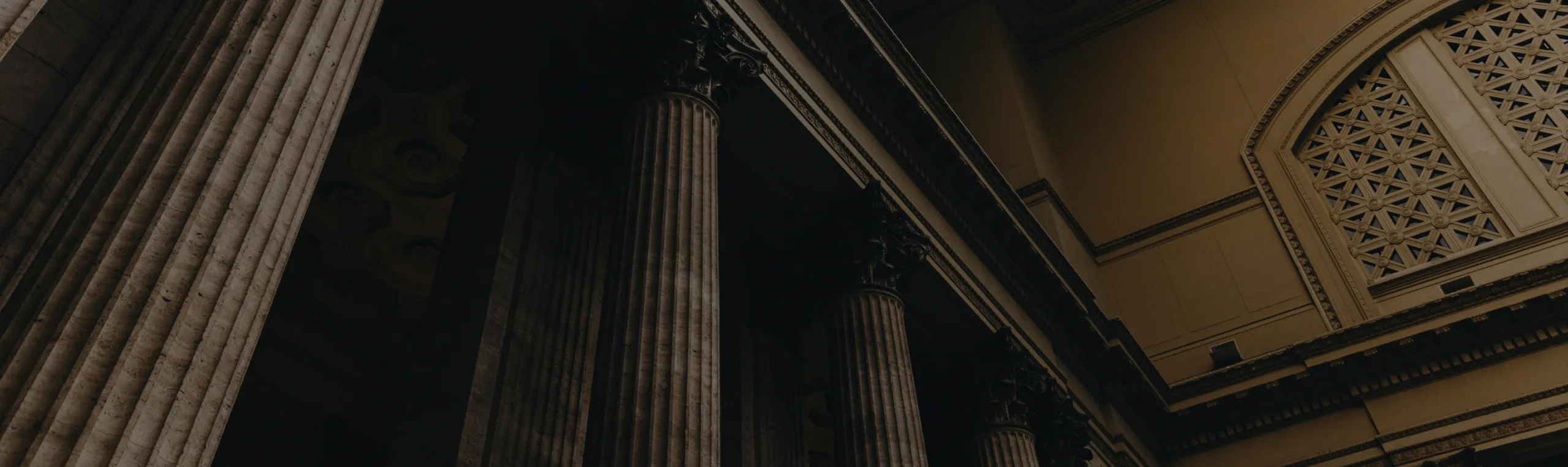 Close-up view of tall, classical stone columns supporting a structure, with intricate architectural details and a dimly lit ambiance, evoking the gravitas one might associate with a court deliberating over a California breach of fiduciary duty case.