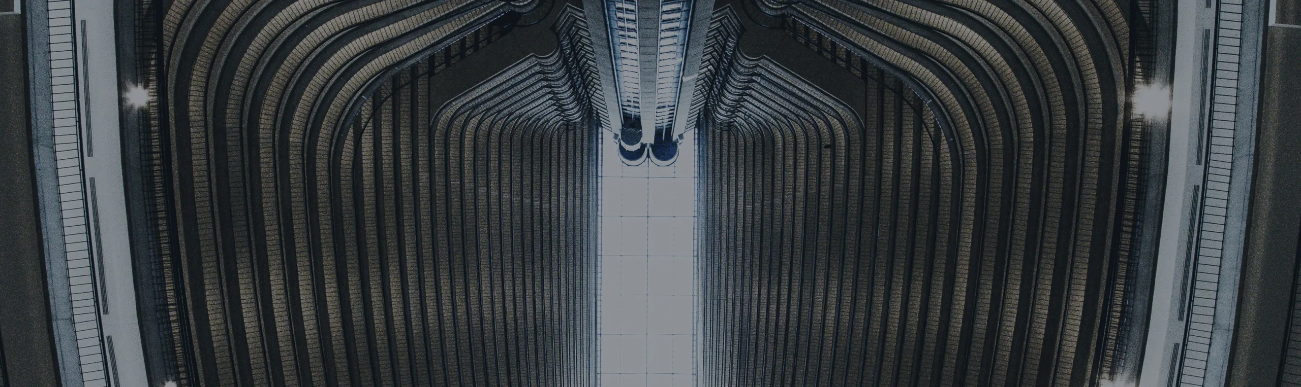 A symmetrical interior view of a multi-story building with curved balconies lining both sides, converging towards a large central atrium filled with natural light from a skylight.