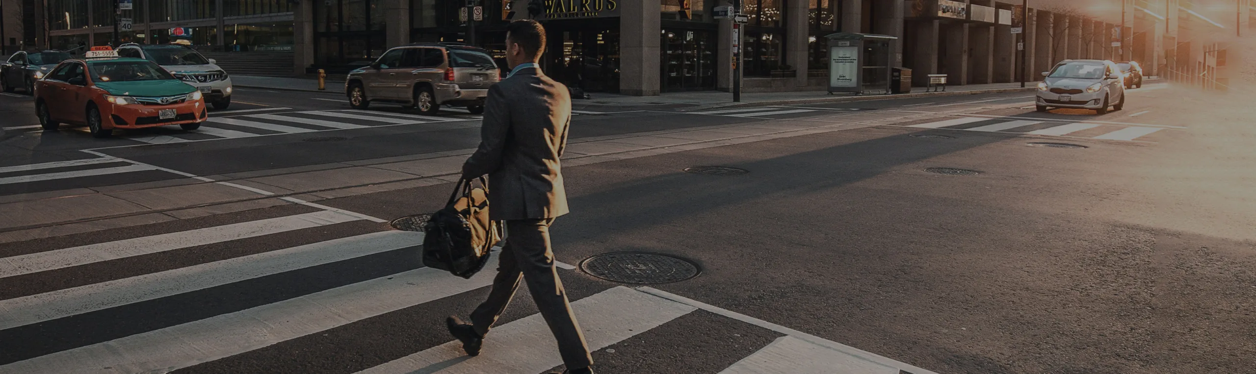 A Los Angeles securities attorney, dressed sharply in a suit, crosses a bustling city street with a briefcase at the crosswalk, as cars pass by in the morning sunlight.