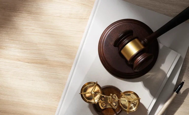 A wooden gavel and a small brass balance scale on a desk next to a notebook and pen.